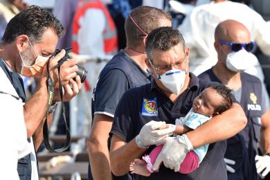 Un funcionario italiano toma una fotografía de un bebé mientras varios migrantes desembarcan de un barco de la Guardia Costera italiana en Pozzallo