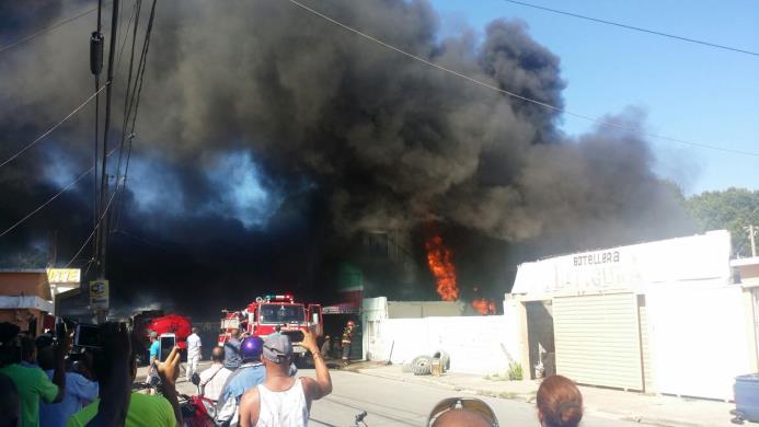 Varios curiosos graban con sus celulares el intenso humo que desprenden las llamas del incendio en una gomera que se incendia en San Pedro de Macorís