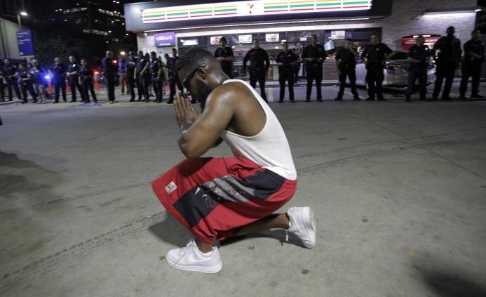 Un joven se arrodilla frente a los policías desplegados en la esquina de Ross Avenue y Griffin street durante una manifestación contra la violencia policial hacia los negros en EEUU.