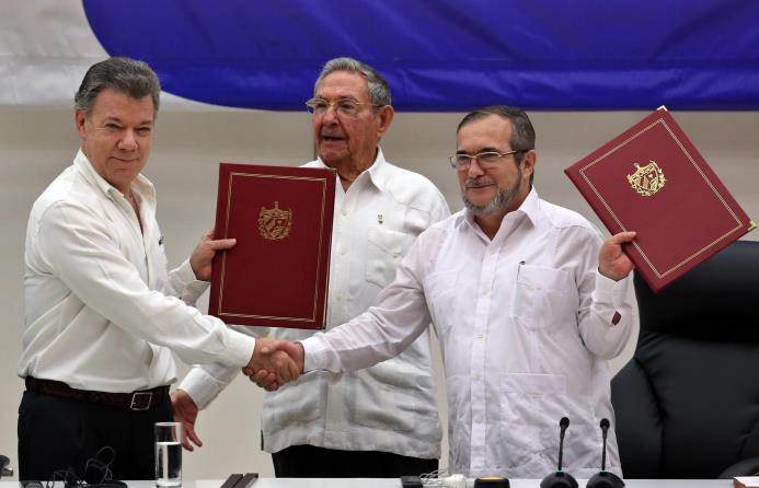El delegado de las FARC en Cuba, Rodrigo Londoño Echeverri, alias "Timochenko" (d) y el presidente de Colombia, Juan Manuel Santos (i) junto a el presidente de Cuba, Raúl Castro (c) sostienen en sus manos el acuerdo de paz entre el Gobierno colombiano y las FARC.