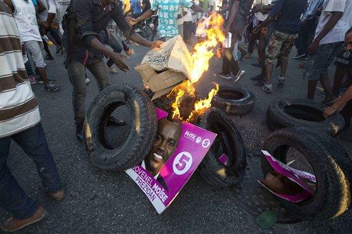 Partidarios de la candidata a la presidencia Maryse Narcisse, del partido político Fanmi Lavalas, queman neumáticos y un cartel del candidato rival Jovenel Moise, del partido PHTK, en Puerto Príncipe, Haití, el lunes 28 de noviembre de 2016. 