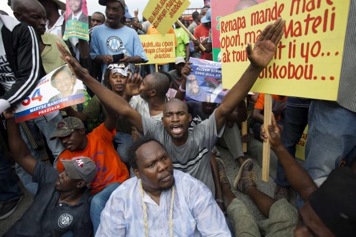 Manifestantes corean consignas opuestas al consejo electoral durante una protesta contra dicho consejo con el fin de conmemorar el 25to aniversario de las primeras elecciones democráticas en el país en 1990, en Puerto Príncipe, Haití, el miércoles 16 de diciembre de 2015. 
