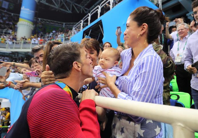 Michael Phelps besa a su esposa Nicole Johnson, que sujeta al hijo de ambos, Boomer, tras ganar su segundo metal dorado. 