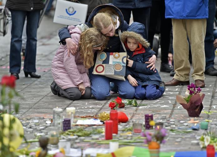 Una mujer y dos niños se sientan en el suelo para recordar a las víctimas de los ataques extremistas en Bruselas, en la plaza de la Bolsa de la capital belga, el 23 de marzo de 2016. 